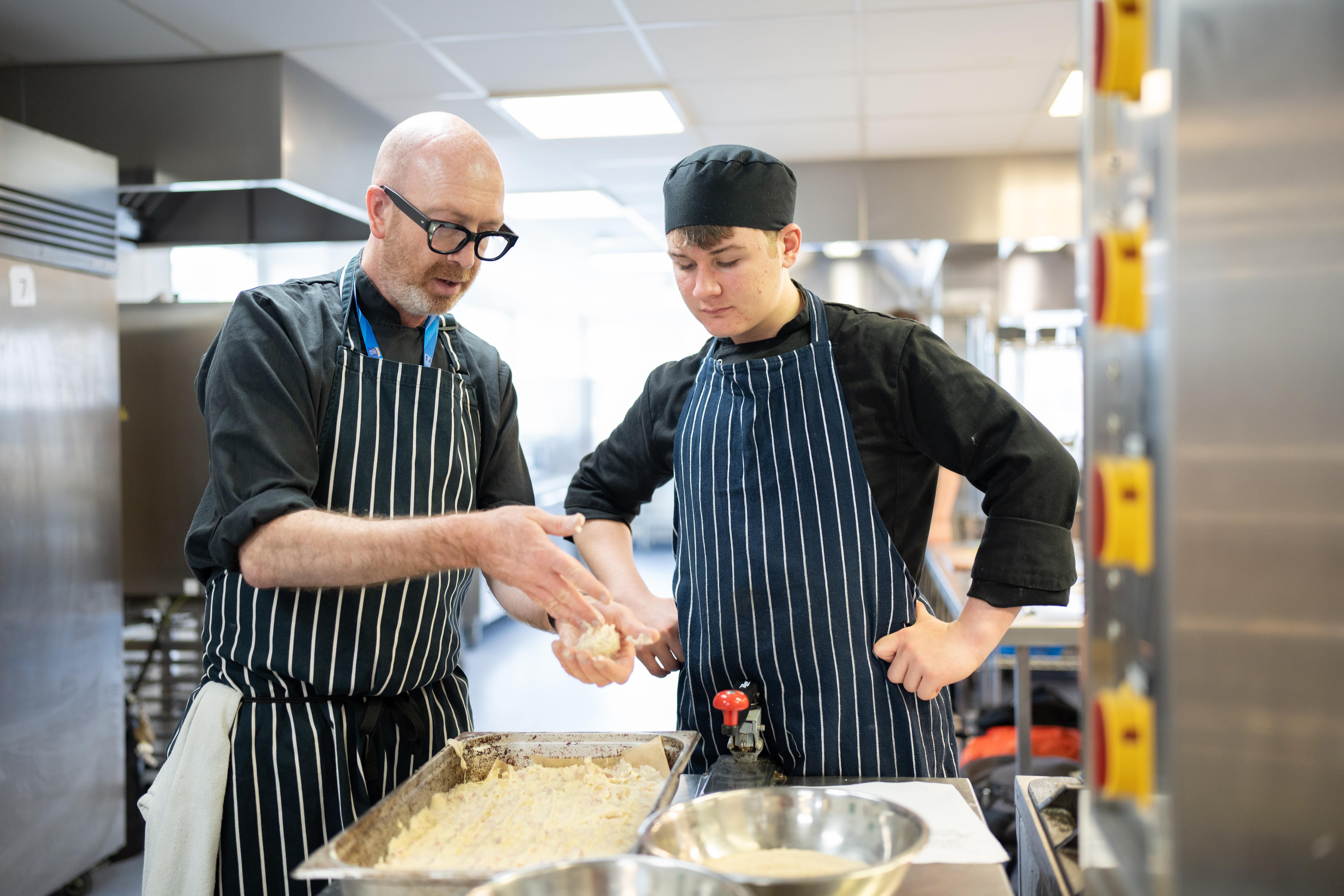 lecturer demonstrates a cooking technique to a student