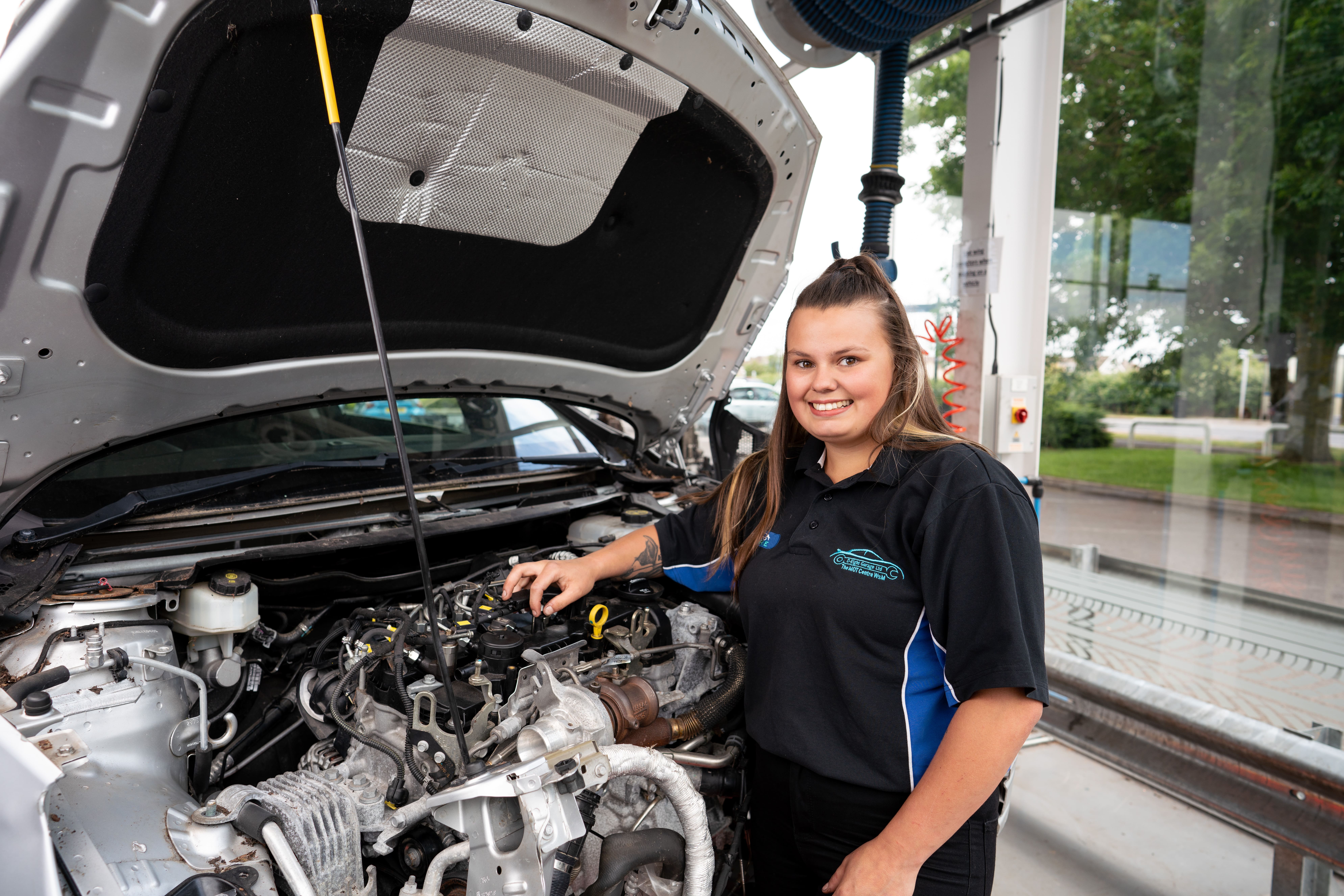 girl poses with a car with its bonnet open