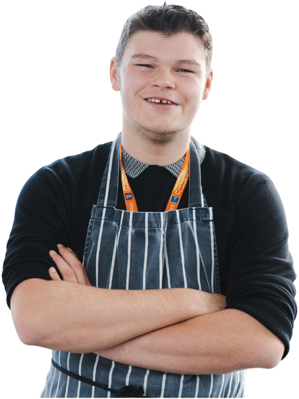 Confident young man wearing a striped apron and a lanyard, smiling with arms crossed against a light background.
