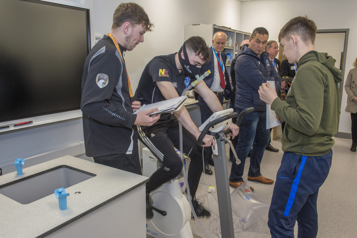 a boy uses a exercise bike while a group watches
