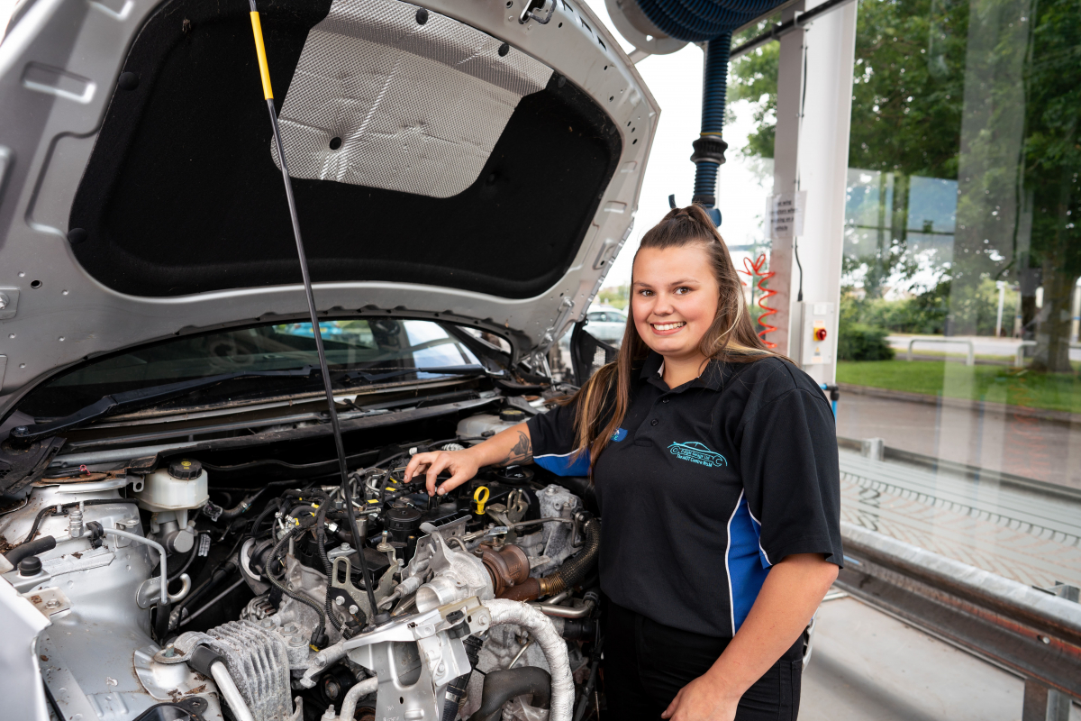 girl poses with a car with its bonnet open