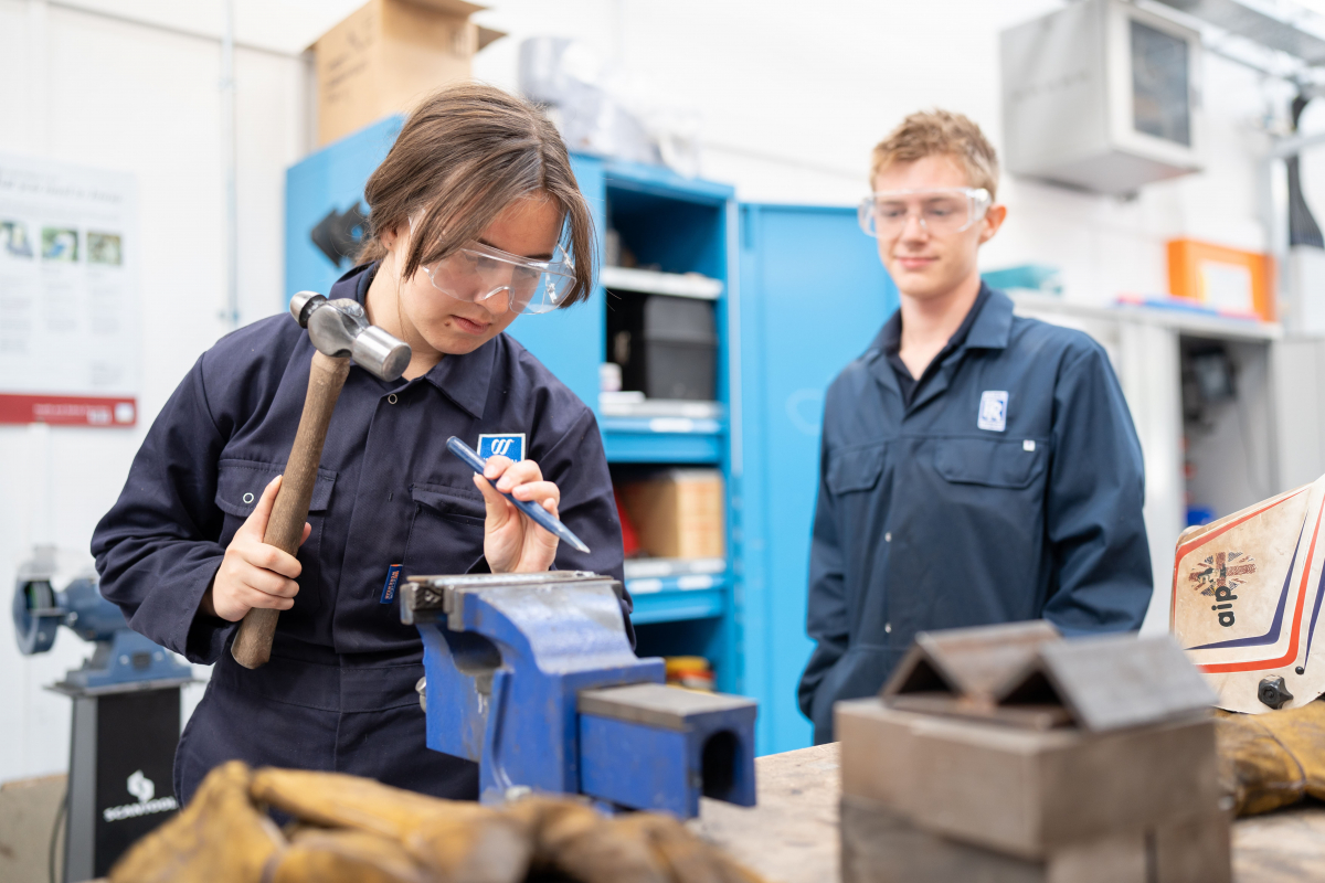 student using chisel and hammer on object in a vice