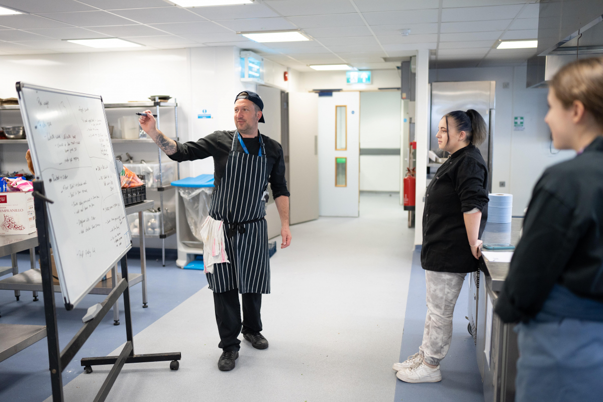 Lecturer explaining something on a flip chart to a student in training kitchen