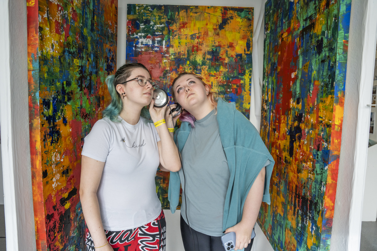 a couple of people standing in front of a painting, listening too some headphones