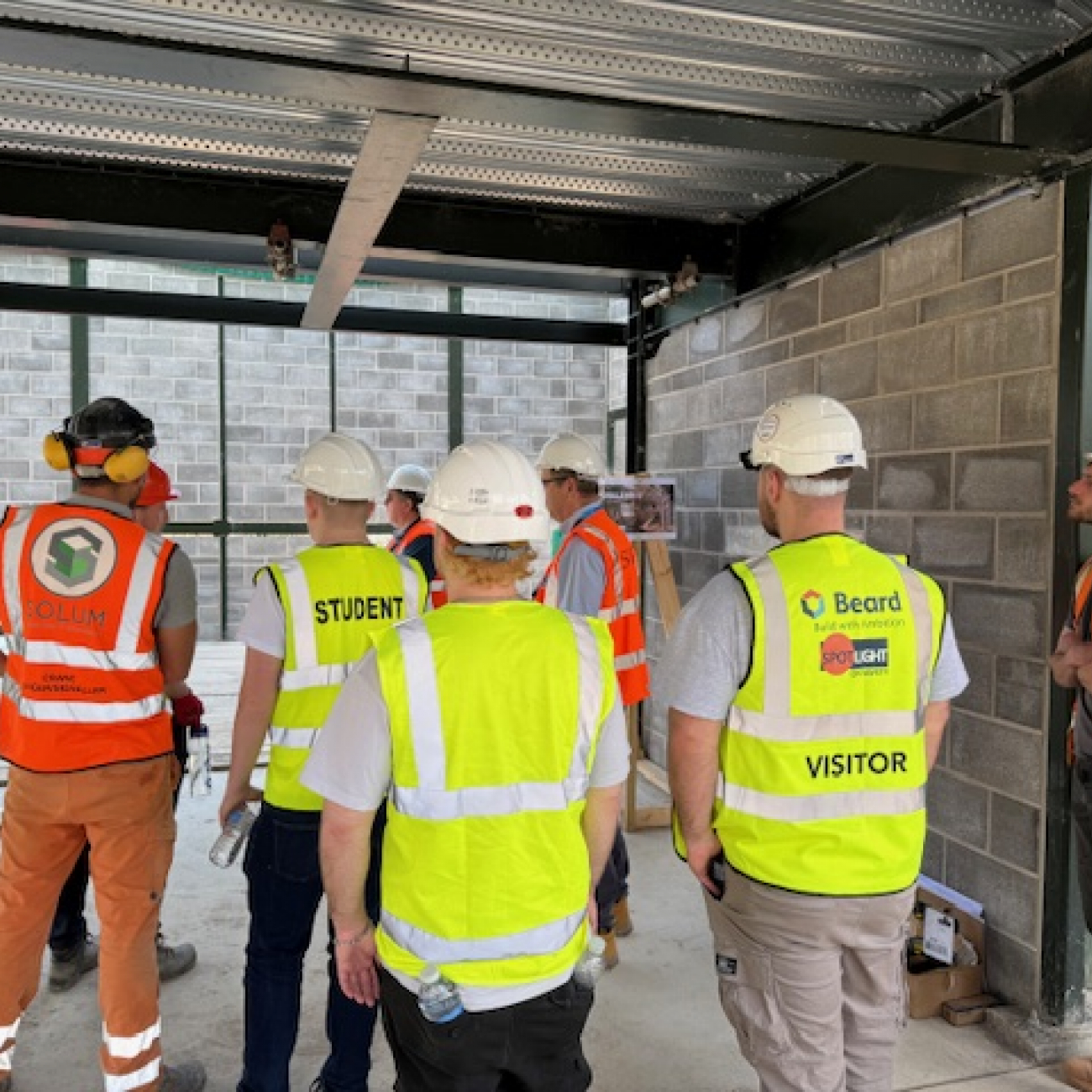 Construction students with high vis' and hard hats on listening to professionals on site