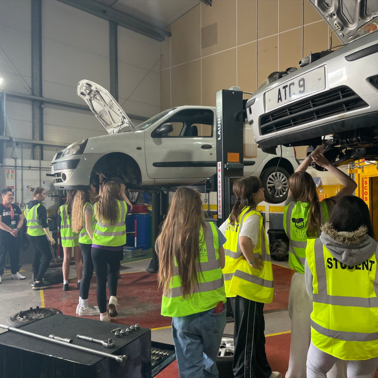 Students in Hi-Vis jackets fixing the underside of a car